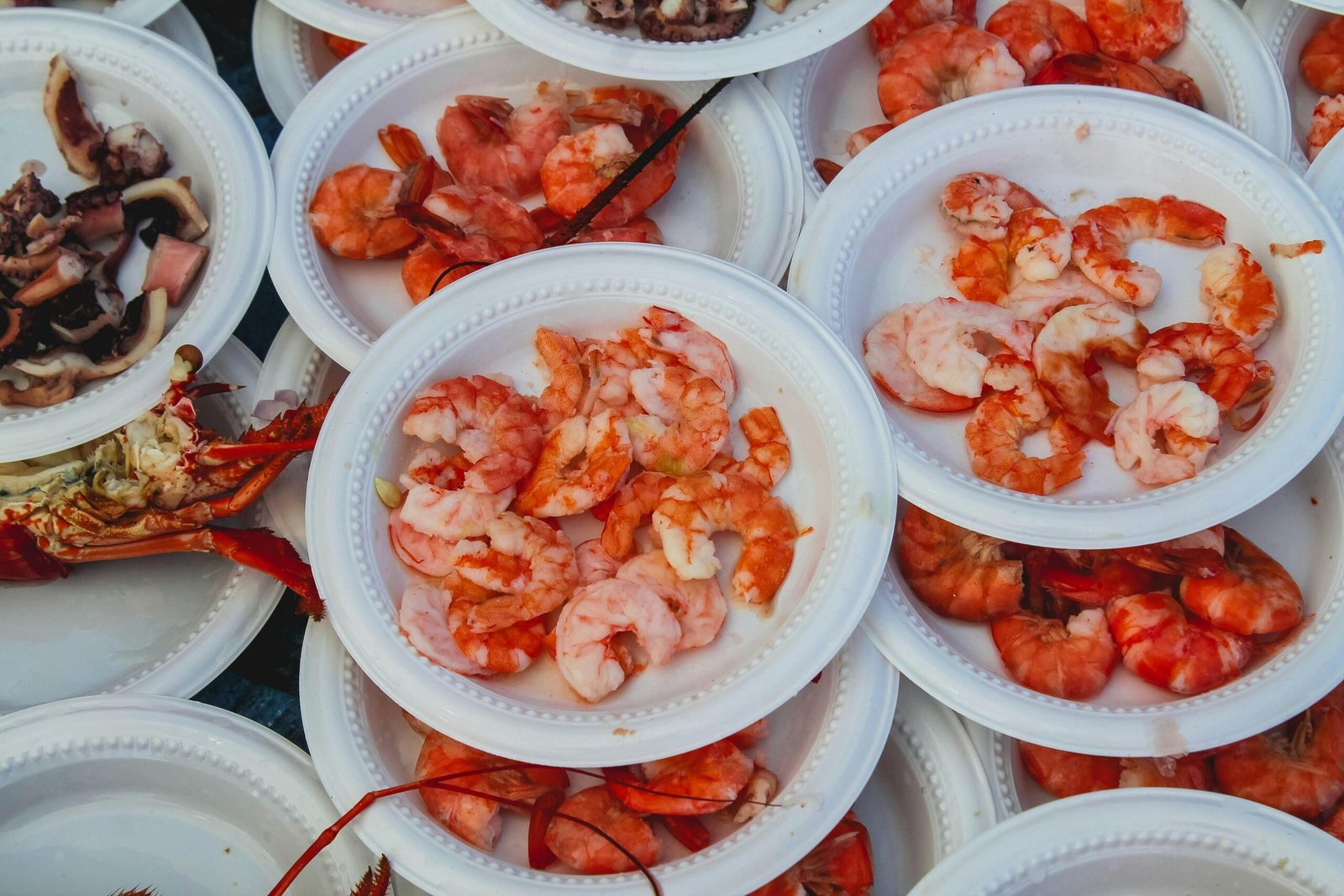 A variety of shrimp dishes served on disposable plates at an outdoor seafood market.