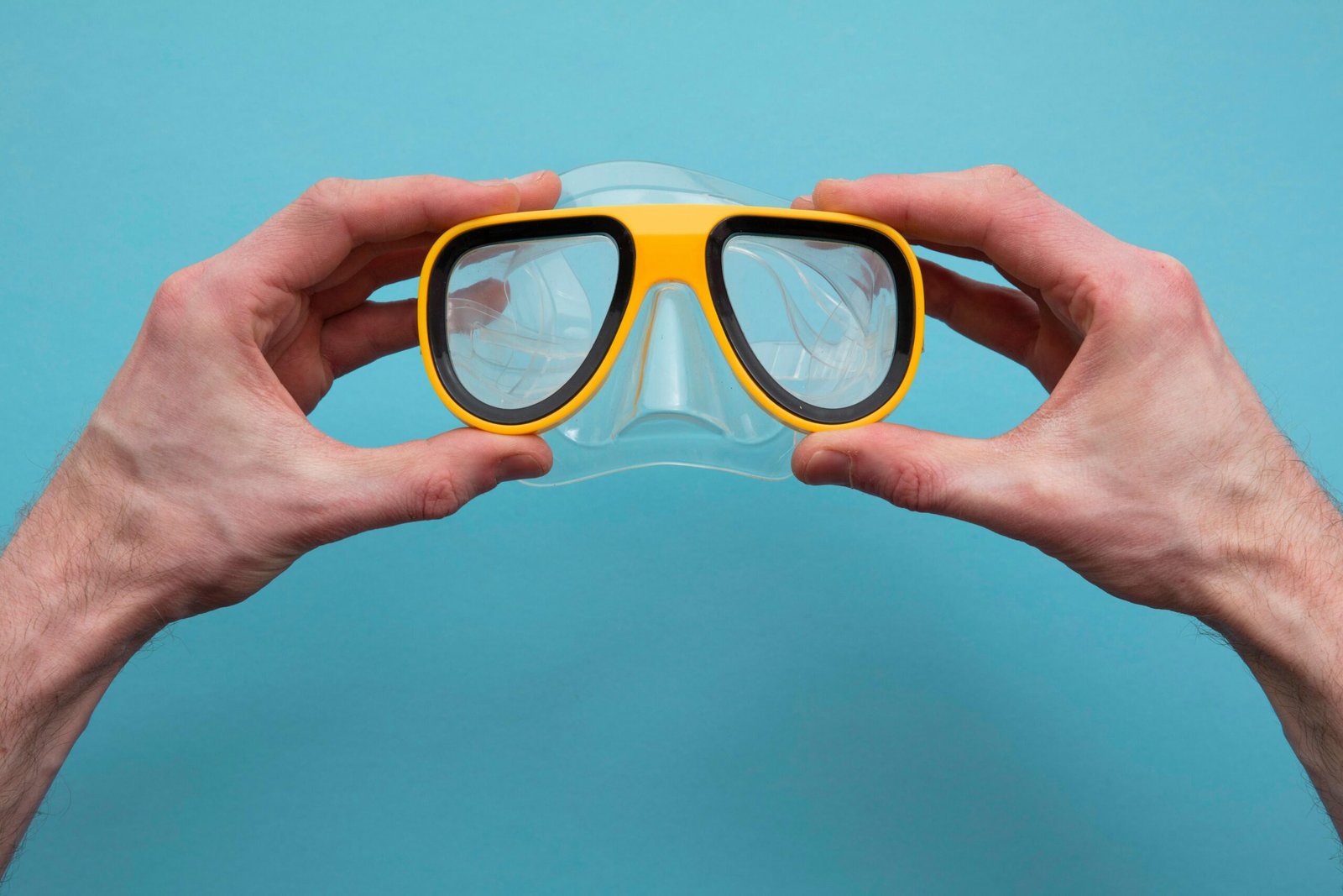 A close-up of hands holding a yellow snorkeling mask against a bright blue background.